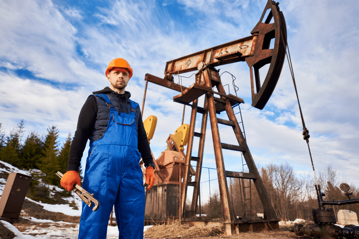 An oil worker standing next to a pump jack, illustrating the human element in oil extraction and the rugged conditions of the job.
