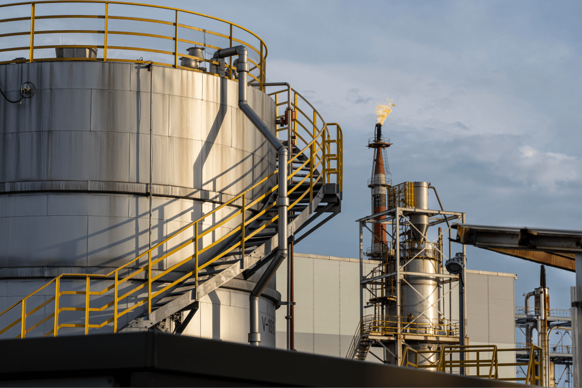 Close-up of storage tanks and a flare stack at an oil refinery, showing the crucial components of oil storage and gas flaring processes.